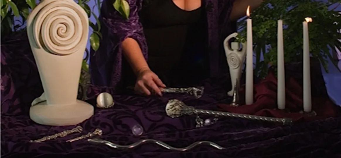An altar with spiral goddess statues, candles, a crystal ball and Willowroot pewter wands on purple velvet